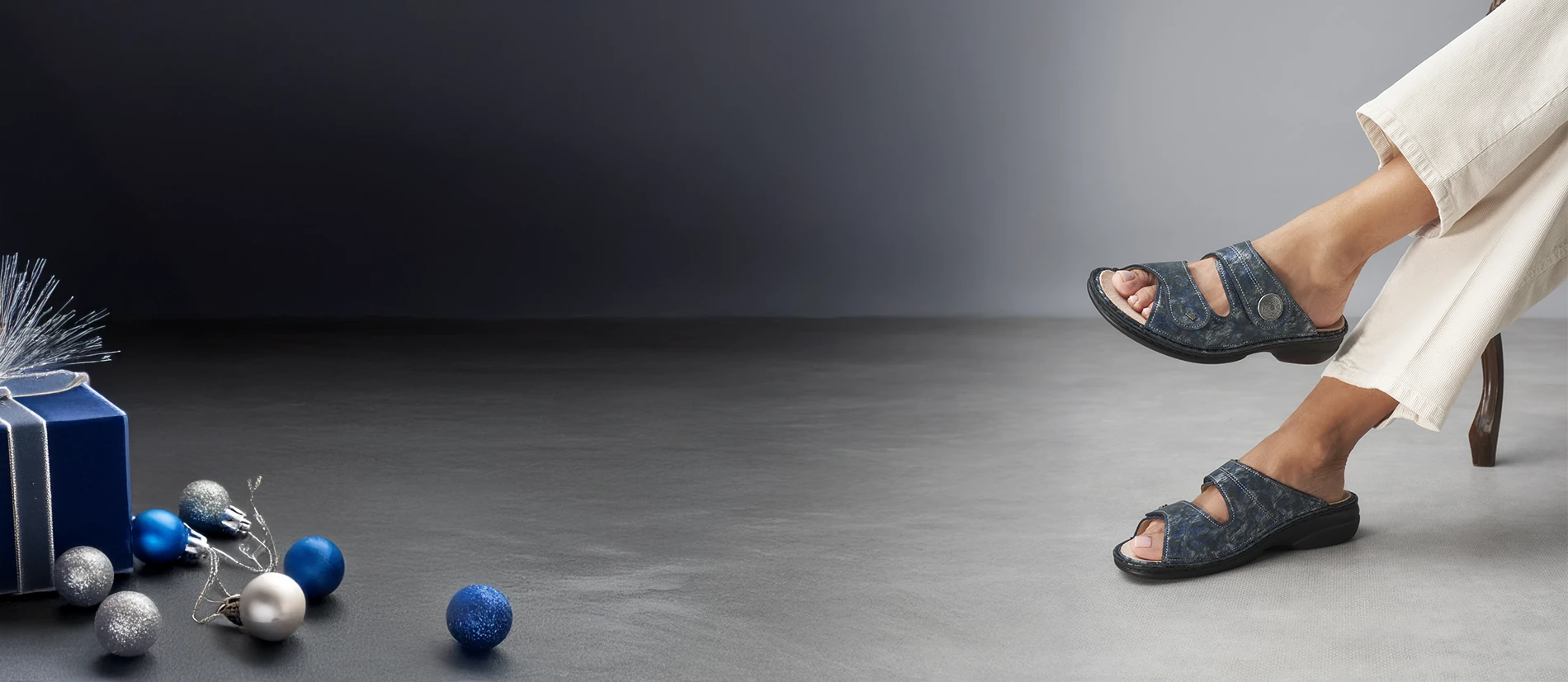 Ciabatte sansibar marine indossate da donna seduta con palle di natale e pacchetto regalo blu argento