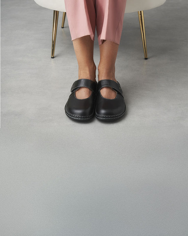 Primo piano di sabot finncomfort Stanford Donna schwarz nere indossate da donna seduta con pantaloni rosa.