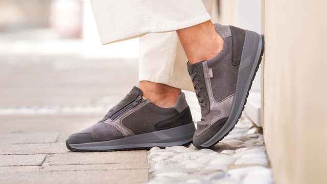 Primo piano laterale di Scarpe Finncomfort Mori grigio mouse indossate da donna con un piede appoggiato su un muretto e uno per terra