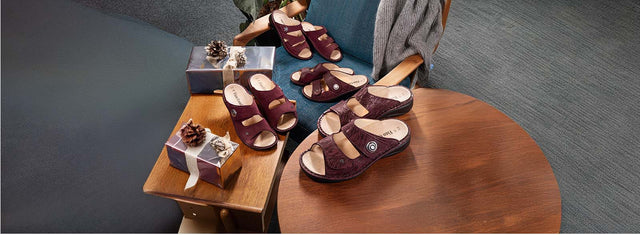 composizione di ciabatte finncomfort bordeaux appoggiate su tavolino in legno, poltrona, tutte di colore bordeaux