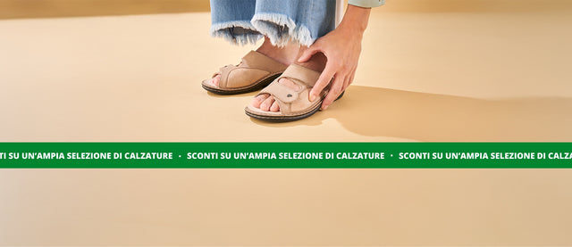 Finncomfort sconti estivi su un'ampia selezione di calzature. Nell'immagine, primo piano del sandalo Sarezzo beige, indossato da donna con jeans che accarezza la calzatura.