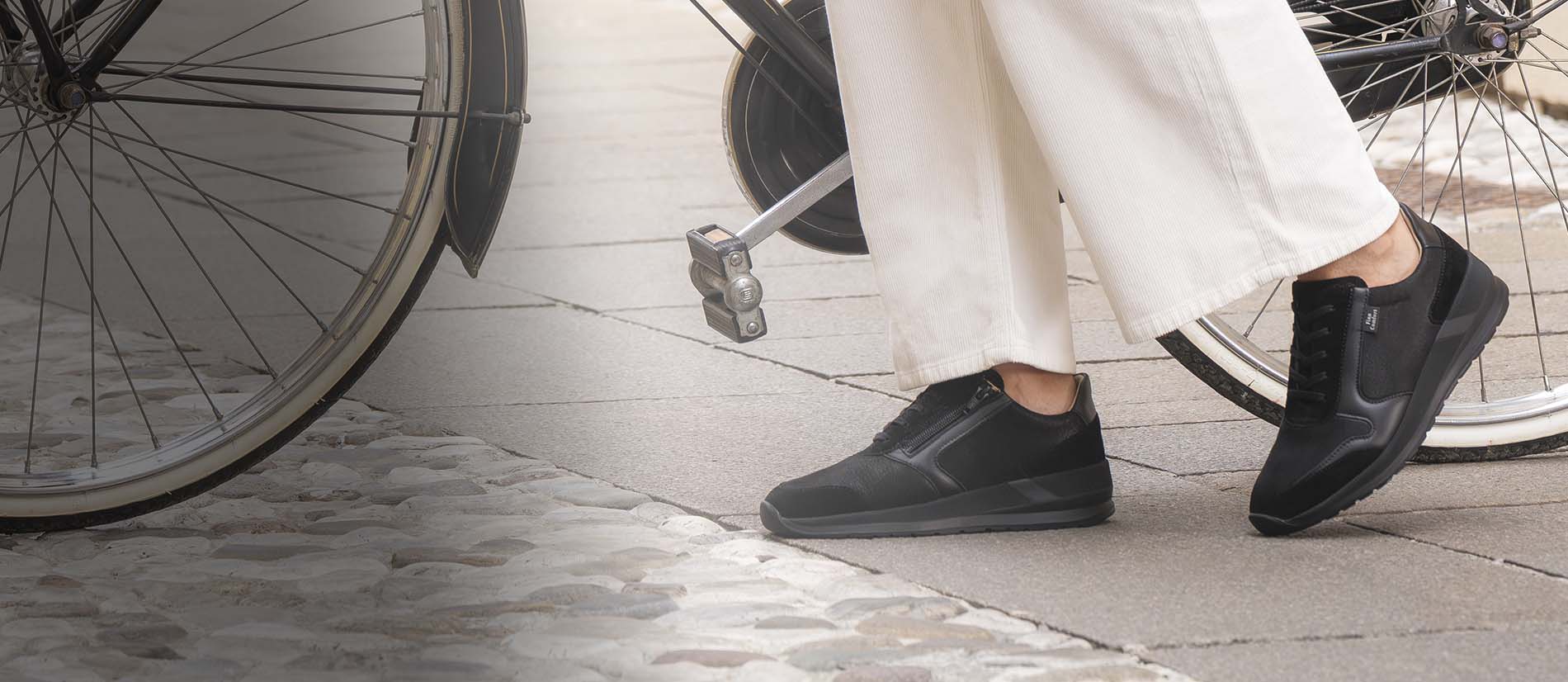 Primo piano di scarpe finncomfort mori nere indossate da signora che sta spingendo una bicicletta nera