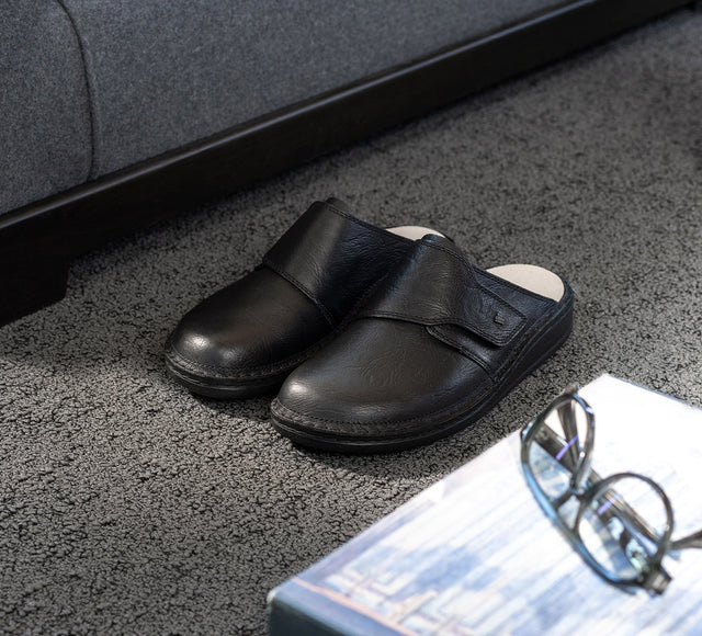primo piano stills di sabot uomo finncomfort in pelle nera appoggiate su moquette grigia