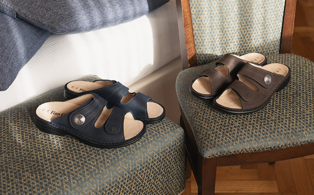 primo piano di ciabatte donna finncomfort  sansibar in colore blu e un paio in color marrone appoggiate su sedia