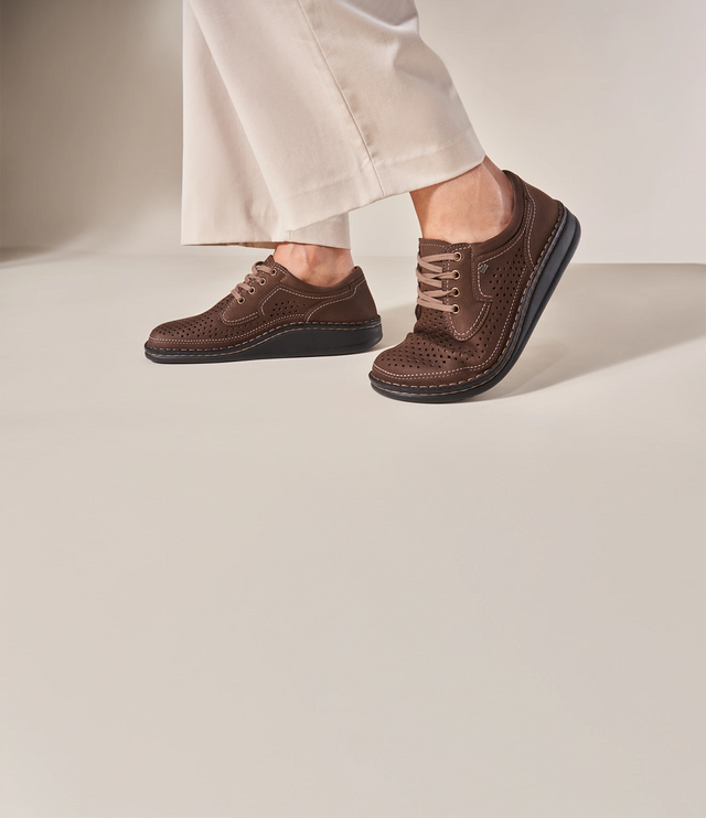 Primo piano indossato di scarpe uomo finncomfort modello baden marrone traforato indossato da uomo con pantaloni bianchi