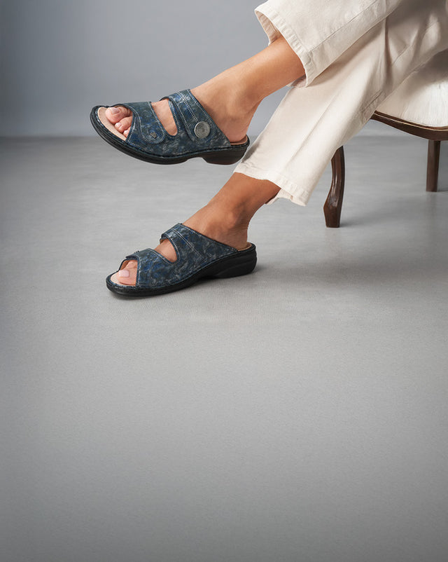 Primo piano di ciabatte pianelle Finncomfort color marine indossate da una donna seduta su una poltrona in stile classico